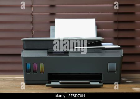 One black printer with sheet of paper on wooden table indoors, closeup Stock Photo