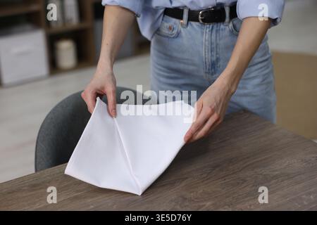 Place setting. Woman putting white napkin onto wooden table at home, closeup Stock Photo