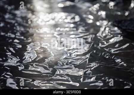 A high-contrast macro shot of a wrinkled, reflective silver surface featuring sharp details and soft bokeh. This versatile abstract texture evokes a s Stock Photo