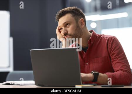 Man Looking Stressed While Working on Laptop in a Modern Office Environment Stock Photo