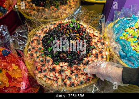 Halloween gummy eyeballs and spooky candy display. Close-up of a Halloween candy stall with gummy eyeballs, creepy insect sweets, and a gloved hand Stock Photo