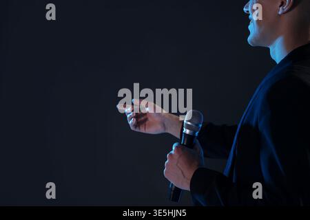 Happy presenter with microphone performing on dark background, closeup. Space for text Stock Photo