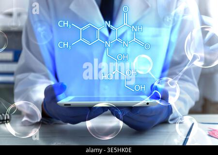 Scientist holding tablet computer at table in laboratory, closeup. Skeletal formula above device. Biochemistry research Stock Photo
