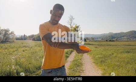 Skincare routine during summer outdoor activities in the countryside, an African American man applying sunscreen to protect his skin from harmful UV Stock Photo