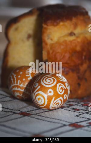 A festive Easter composition featuring two brown eggs decorated with white patterns and a sliced sweet Easter bread (paska) on a traditional embroider Stock Photo