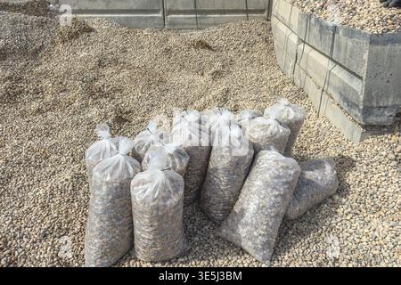 Transparent plastic bags filled with small gravel stones placed on a pile, construction and landscaping materials prepared for outdoor ground covering Stock Photo