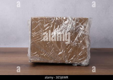 Cardboard box in plastic wrap on wooden table, closeup Stock Photo