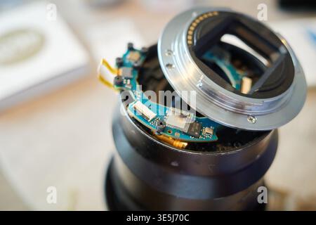 This close-up shows a camera lens with a broken mount after a drop. The detached metal ring exposes the internal circuit board and ribbon cables. Stock Photo