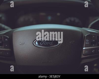 Close-up view of a Ford steering wheel hub with central logo, horn icons, airbag marking, and multi-function control buttons in a car interior Stock Photo