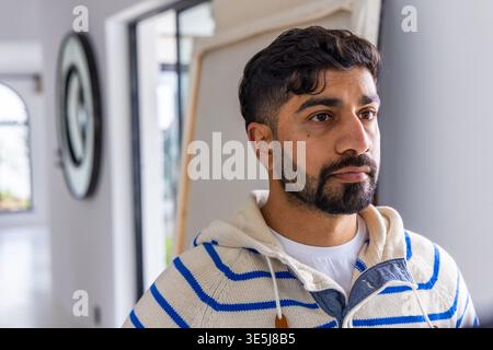 Male standing right in home hallway wearing cream striped hoodie and white tee, canvas leaning Stock Photo