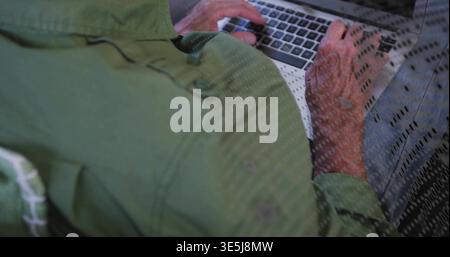 Typing senior man wearing green jacket, jeans at home, using silver laptop with dotted overlay Stock Photo