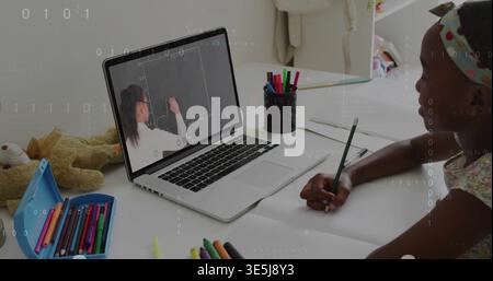 Working kid in printed top, headband, writing with pencil viewing laptop lesson at desk, copy space Stock Photo