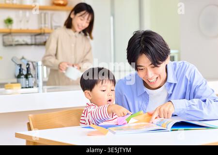 Japanese father teaching his toddler son origami at home in the dining room enjoying family time Stock Photo