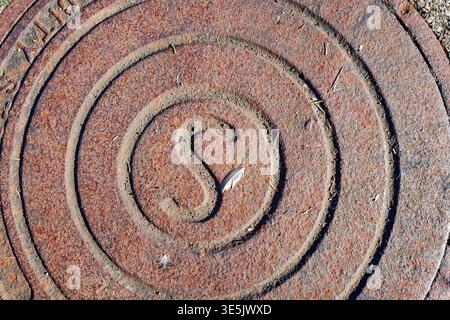 A rusty metal sewer cap on the ground with a small bird feather Stock Photo