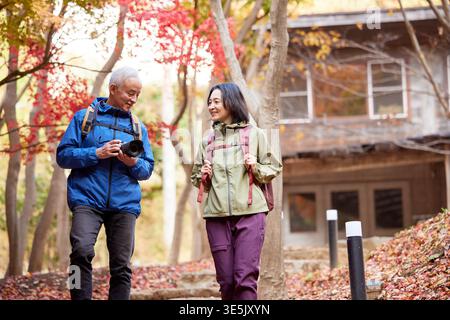 Smiling Japanese senior couple on autumn hike with camera Stock Photo