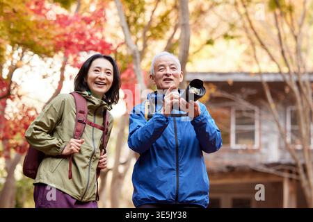Japanese senior couple taking photos and smiling on an autumn hike Stock Photo
