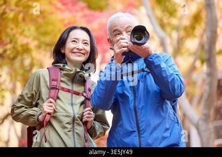 Smiling Japanese senior couple taking photos on an autumn hike Stock Photo