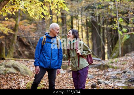 Happy Japanese senior couple hiking in an autumn forest Stock Photo