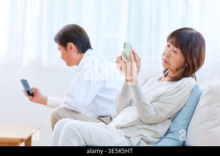 Japanese senior couple concentrating on smartphones in living room Stock Photo