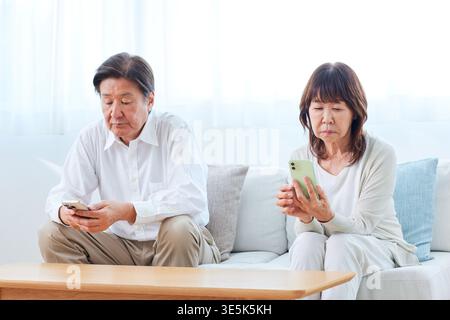 Silent Japanese senior couple using smartphones in the living room Stock Photo