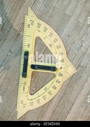 Riga, Latvia - March 31, 2026:Top view of a large transparent protractor with triangle rulers on a wooden floor. Ideal for education, geometry, engine Stock Photo