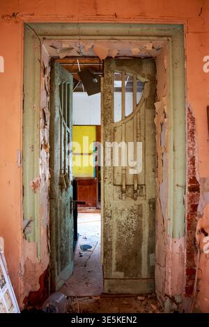 Decaying doorway with peeling paint and exposed brick opens into rooms with vibrant contrasting colors and debris strewn about Stock Photo