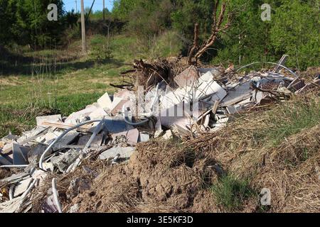 Illegal construction debris dump piled up in a grassy, wooded area under bright spring sunlight Stock Photo