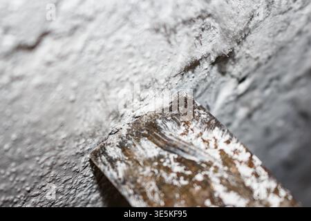 Close-up shot revealing efflorescence crystals forming needle-like deposits on a damp basement concrete wall surface near a scraping tool Stock Photo