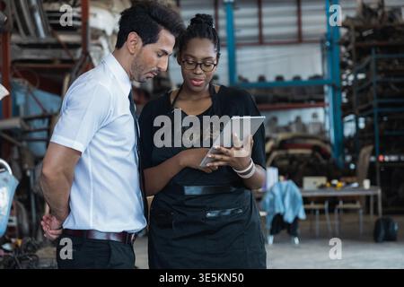 Diverse business partners using tablet to check auto parts in industrial warehouse storage Stock Photo
