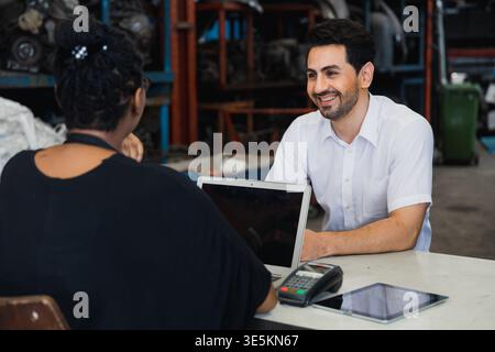 Customer consulting with mechanic at auto repair shop counter using laptop Stock Photo