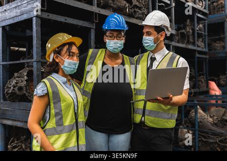 Diverse workers in face masks with laptop discussing inventory in auto parts warehouse Stock Photo