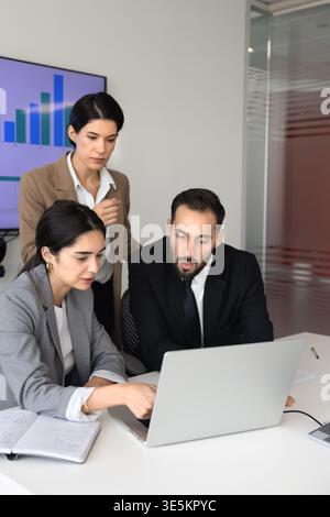 Team analyzing data, discussing corporate strategy on laptop in office Stock Photo