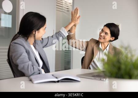 Businesswomen reaching corporate goal, exchanging high five in office Stock Photo