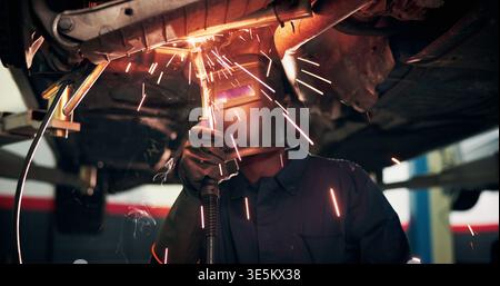 Mechanic, welding and person with tools by car for diagnostics, maintenance or auto service. Workshop, sparks and technician with equipment for Stock Photo