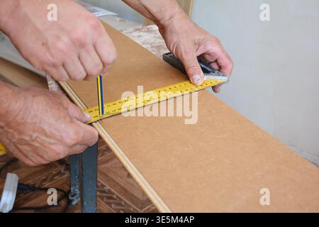 Workers installing wooden laminate flooring and measuring laminate board before cutting. Stock Photo