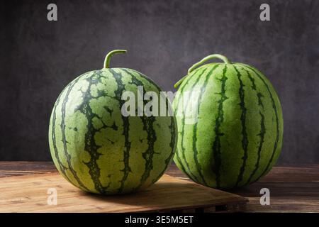 Two green striped watermelons resting on a cutting board and rustic wooden surface Stock Photo