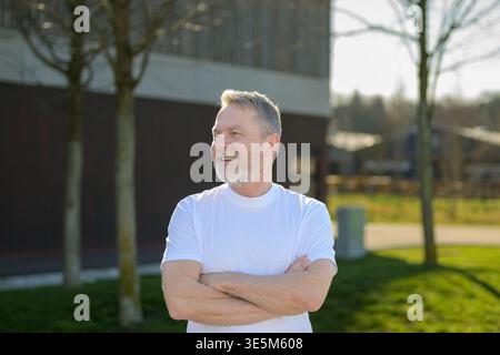 Portrait of a confident mature man standing outdoors with crossed arms in natural sunlight. Stock Photo