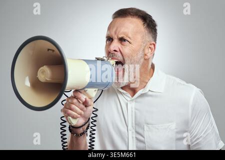 Angry, businessman and shouting on megaphone in studio for authority, control and verbal harassment. Bullhorn, mature manager and yell on white Stock Photo
