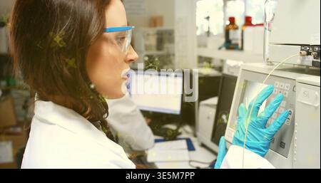 Operating lab tech using instrument keypad tubing at lab bench wearing coat goggles and blue gloves Stock Photo
