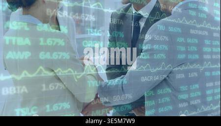Shaking hands four executives wearing suits and light blazer in office, with stock tickers overlay Stock Photo