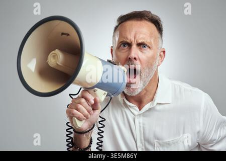 Angry, businessman and scream on megaphone in studio for authority, control or verbal harassment. Portrait, mature manager or bullhorn on white Stock Photo