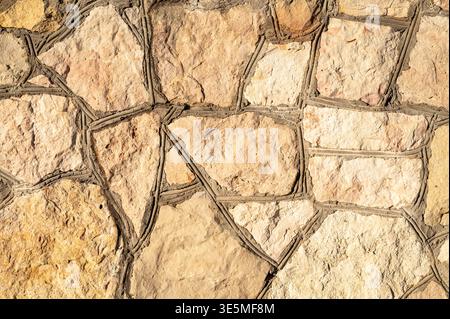 Natural stone wall texture background with irregular beige stones and gray cement joints. Close up of decorative rock masonry and facade Stock Photo