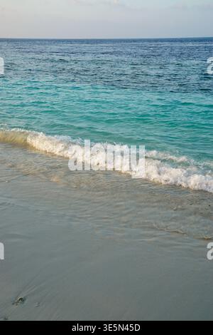 Small waves breaking onto a sandy beach with turquoise ocean water and calm sea stretching to the horizon. Stock Photo