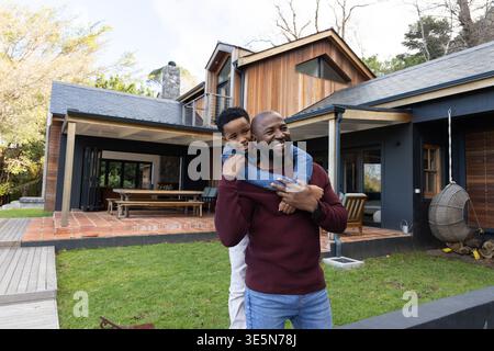 African American father and son playing, father carrying child on back near wooden house patio Stock Photo