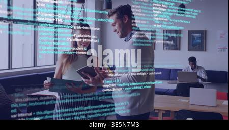 Discussing pair wearing business attire holding tablet, phone and prints in workspace code overlay Stock Photo