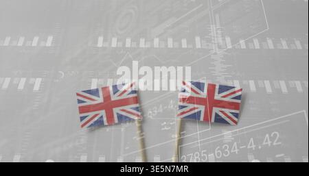 Displaying two Union Jack flags on wooden sticks leaning on gray surface, faint financial overlay Stock Photo