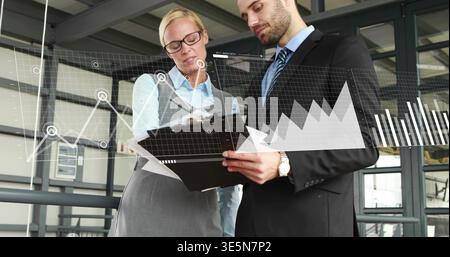 Reviewing professionals in suits examining black clipboard on mezzanine, showing data overlays Stock Photo