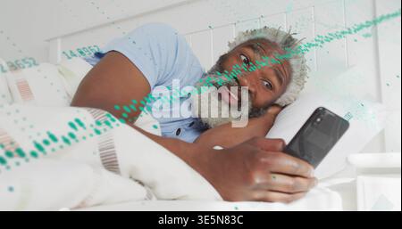 Lying senior man wearing blue shirt, holding phone watching screen in bedroom, green waveform Stock Photo