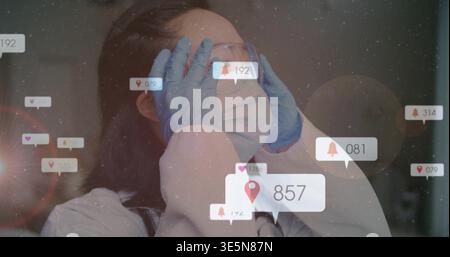 Korean doctor adjusting goggles in clinic, wearing mask gloves lab coat stethoscope with UI icons Stock Photo