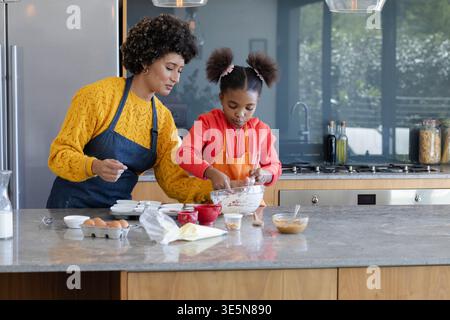 Mixing Diverse mother and daughter at marble countertop in home kitchen, using glass mixing bowl Stock Photo